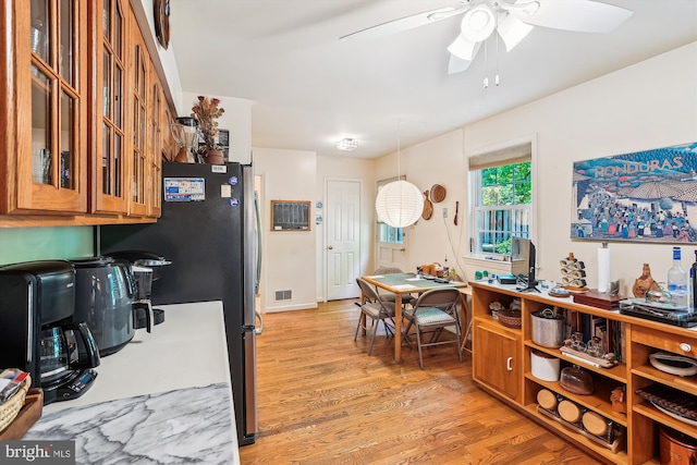 kitchen with freestanding refrigerator, glass insert cabinets, a ceiling fan, and light wood finished floors