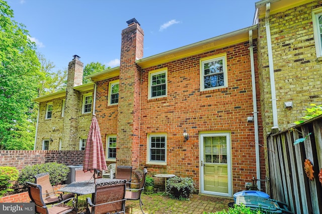 rear view of property with brick siding, a chimney, fence, and a patio
