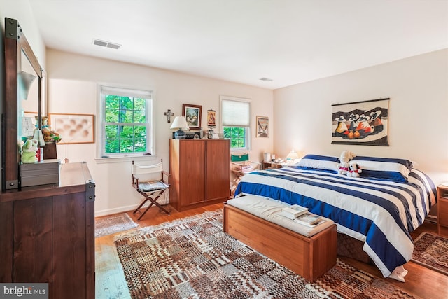 bedroom with baseboards, visible vents, and wood finished floors