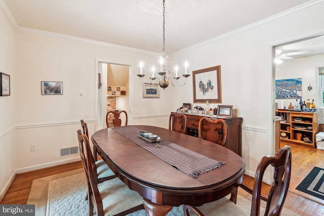 dining space featuring ornamental molding, light wood-style flooring, ceiling fan with notable chandelier, and visible vents