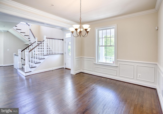unfurnished dining area featuring an inviting chandelier, ornamental molding, wainscoting, stairway, and dark wood finished floors