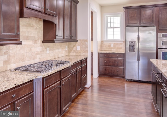 kitchen with dark wood-style flooring, dark brown cabinets, light stone countertops, backsplash, and stainless steel appliances