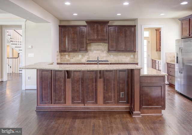 kitchen featuring dark wood finished floors, decorative backsplash, a kitchen island with sink, and stainless steel refrigerator with ice dispenser