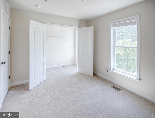 unfurnished bedroom featuring visible vents, a closet, multiple windows, and light colored carpet