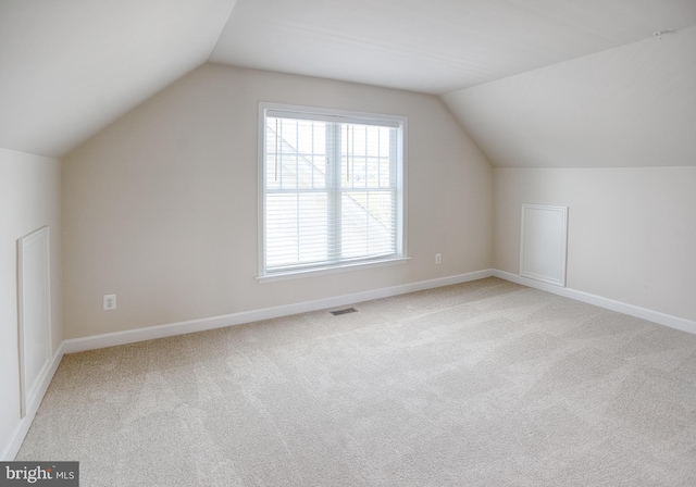 additional living space with baseboards, lofted ceiling, light colored carpet, and visible vents