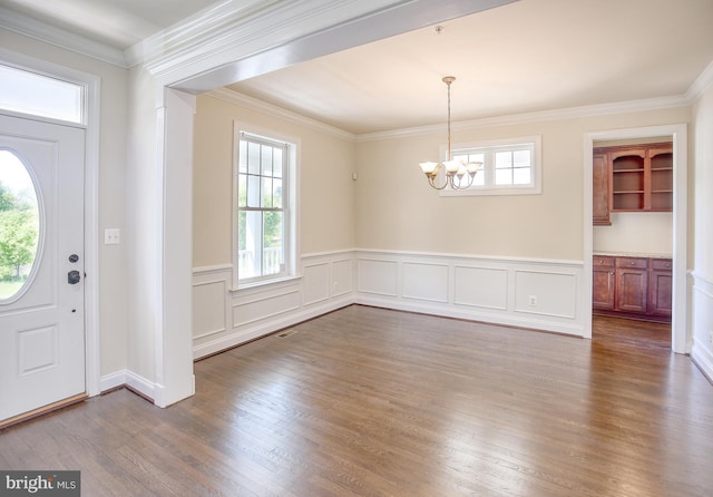 foyer with an inviting chandelier, wainscoting, a wealth of natural light, and dark wood finished floors