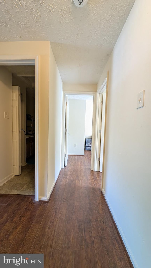 hall with baseboards, a textured ceiling, and dark wood finished floors