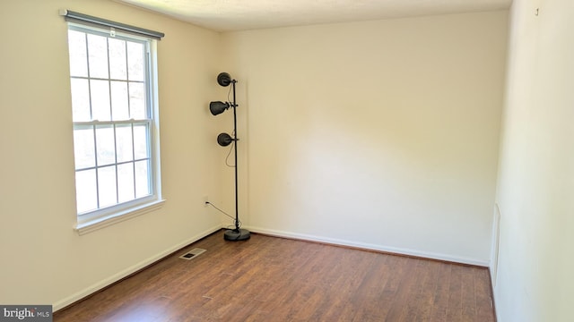 empty room featuring dark wood-style flooring, baseboards, and visible vents