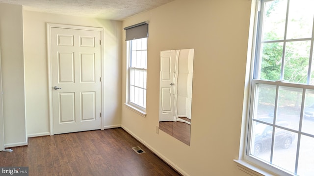 empty room with baseboards, visible vents, a healthy amount of sunlight, and dark wood finished floors