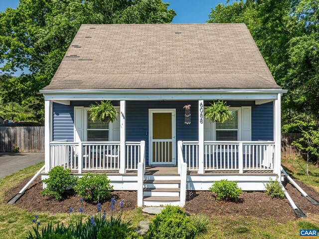 cape cod home with a porch, roof with shingles, and fence