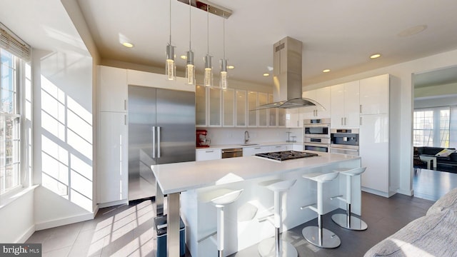 kitchen featuring a breakfast bar, island range hood, light countertops, a sink, and stainless steel appliances