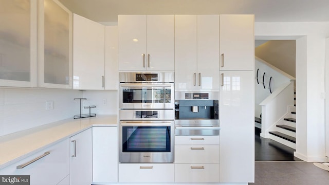 kitchen with white cabinets, stainless steel double oven, light countertops, glass insert cabinets, and a warming drawer
