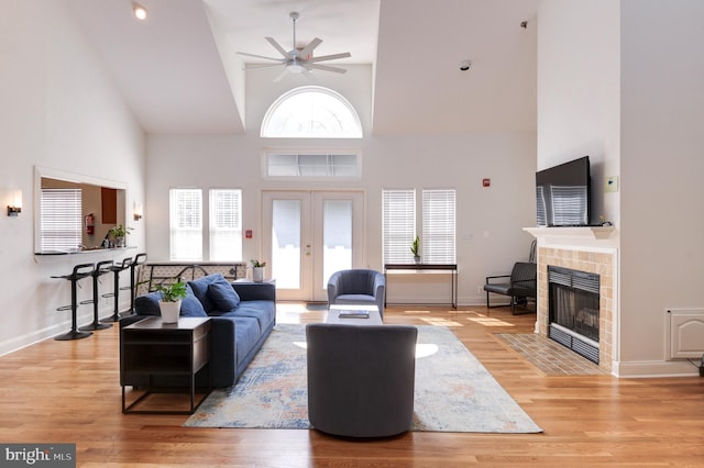 living area featuring high vaulted ceiling, ceiling fan, light wood-style floors, and a tile fireplace