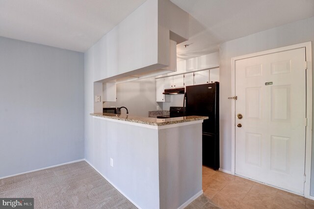 kitchen with a peninsula, light stone countertops, under cabinet range hood, white cabinets, and black appliances