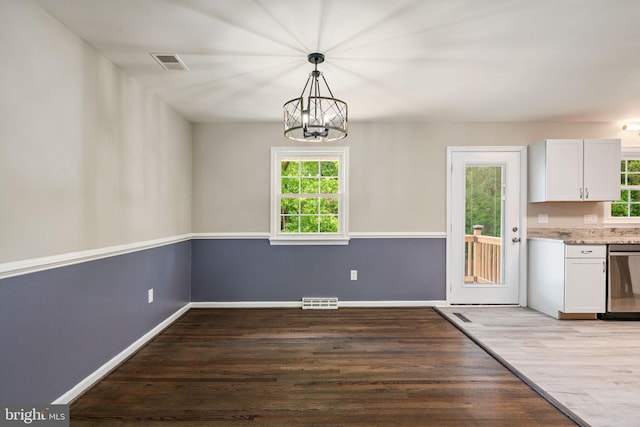 unfurnished dining area with an inviting chandelier, baseboards, wood finished floors, and visible vents