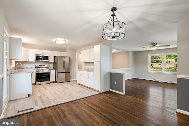 kitchen featuring white cabinetry, ceiling fan with notable chandelier, open floor plan, stainless steel appliances, and light wood-style flooring