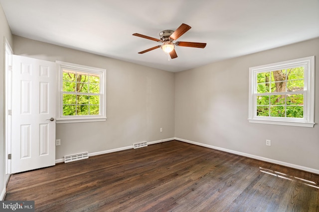 empty room featuring visible vents, a ceiling fan, dark wood finished floors, and a wealth of natural light