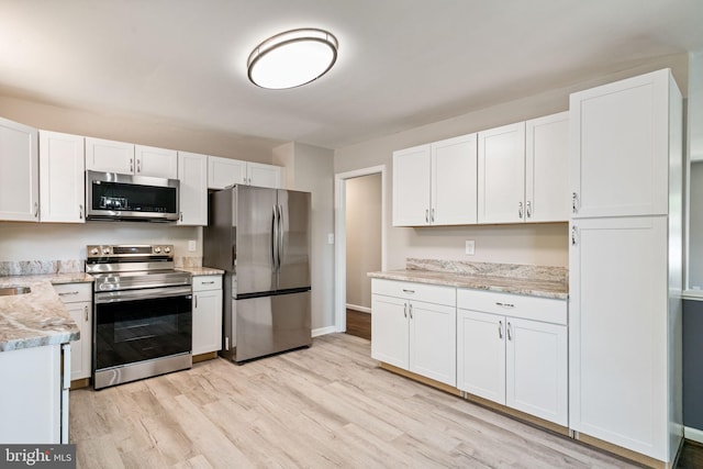 kitchen featuring baseboards, light wood-type flooring, white cabinetry, light stone counters, and appliances with stainless steel finishes