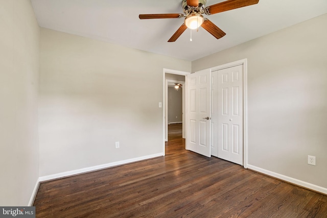unfurnished bedroom featuring dark wood-style flooring, baseboards, ceiling fan, and a closet
