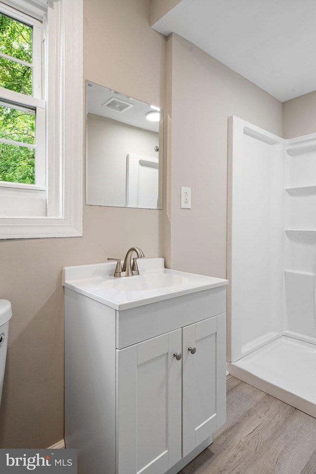 full bathroom featuring vanity, toilet, wood finished floors, a shower, and visible vents