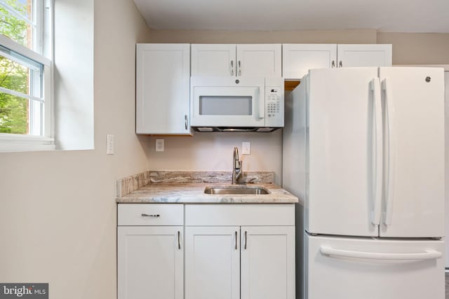 kitchen with white appliances, white cabinetry, light stone counters, and a sink