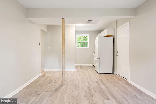 basement featuring freestanding refrigerator, baseboards, visible vents, and light wood-style floors