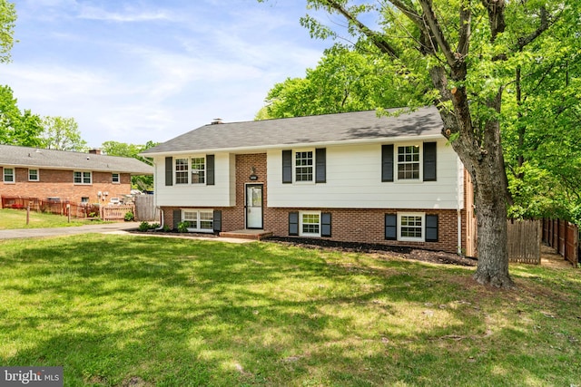 split foyer home featuring brick siding, fence, and a front yard