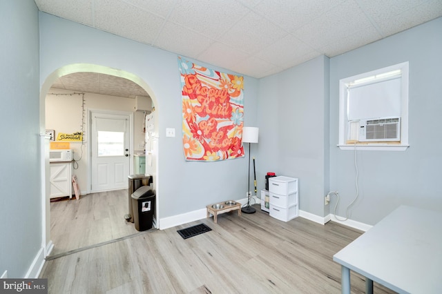 empty room with arched walkways, baseboards, a drop ceiling, wood finished floors, and visible vents