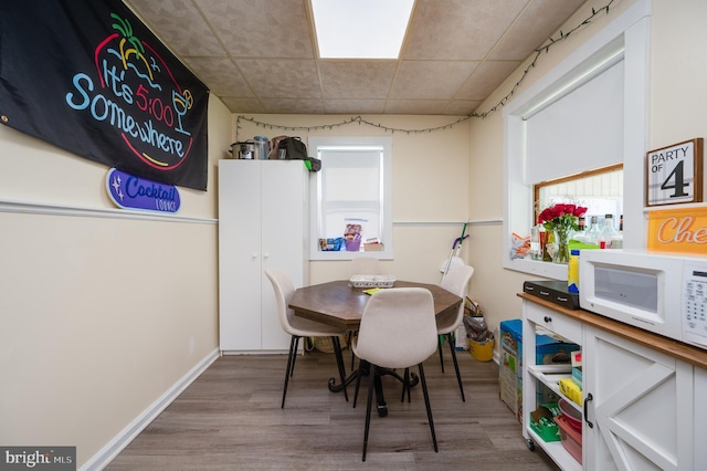 dining space featuring a paneled ceiling, baseboards, and wood finished floors