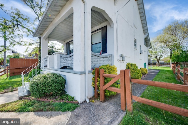 view of side of home with covered porch, fence, and stucco siding