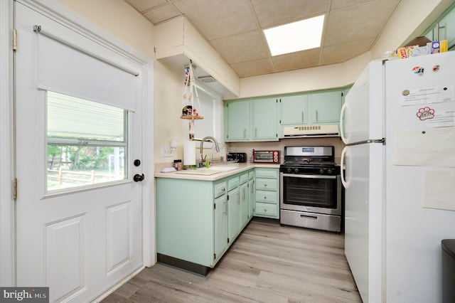kitchen featuring light countertops, freestanding refrigerator, range hood, gas range, and green cabinets