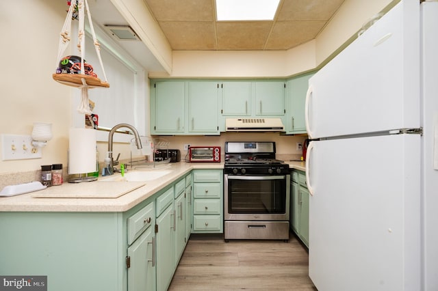kitchen featuring gas stove, green cabinetry, freestanding refrigerator, and exhaust hood