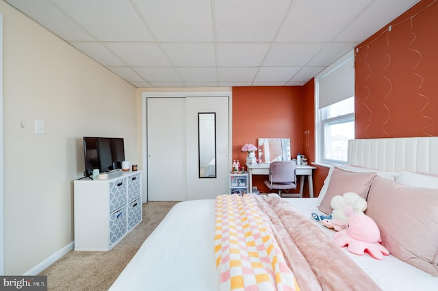 bedroom with carpet flooring, baseboards, a paneled ceiling, and a closet