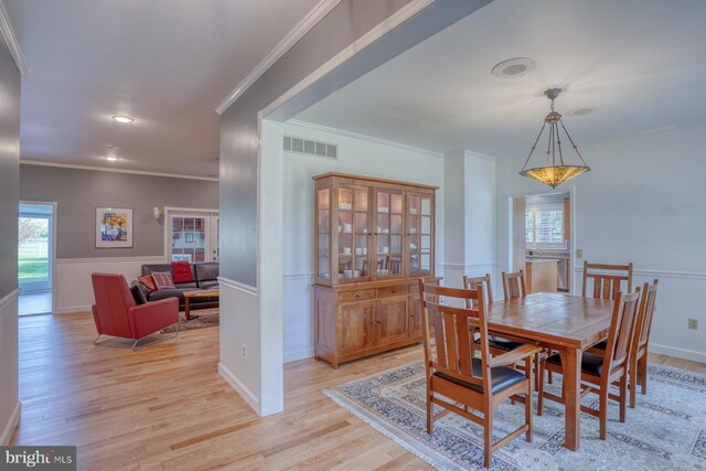 dining area featuring visible vents, light wood-type flooring, baseboards, a wainscoted wall, and ornamental molding