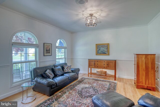 living area with baseboards, ornamental molding, light wood-style flooring, and a notable chandelier