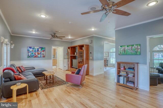 living area with crown molding, a ceiling fan, wood finished floors, and a wainscoted wall