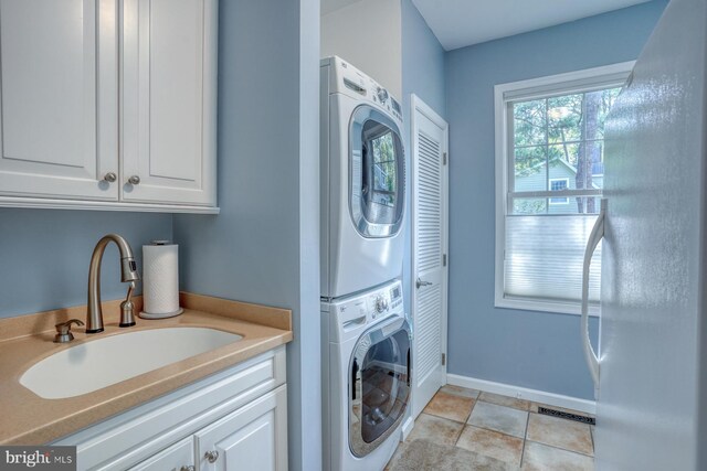 laundry room featuring laundry area, a sink, baseboards, stacked washer / dryer, and visible vents