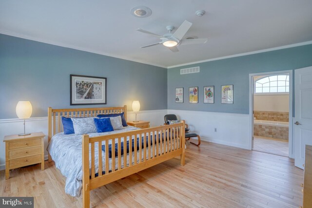 bedroom featuring visible vents, ornamental molding, wood finished floors, ensuite bathroom, and a wainscoted wall