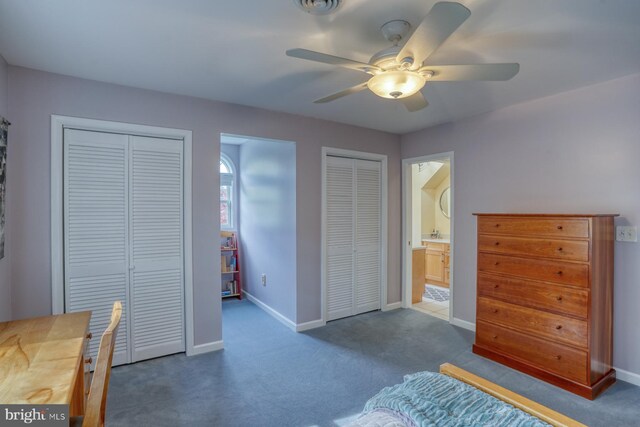 bedroom with carpet flooring, connected bathroom, ceiling fan, two closets, and baseboards