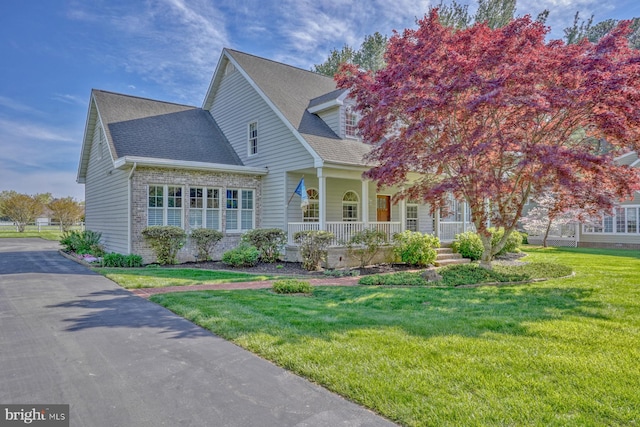 view of front of home with covered porch, brick siding, a shingled roof, and a front lawn