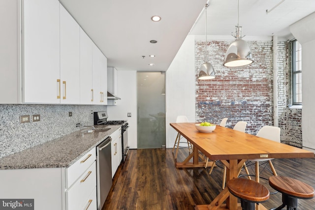 kitchen featuring white cabinets, dark wood-style flooring, light stone countertops, appliances with stainless steel finishes, and brick wall