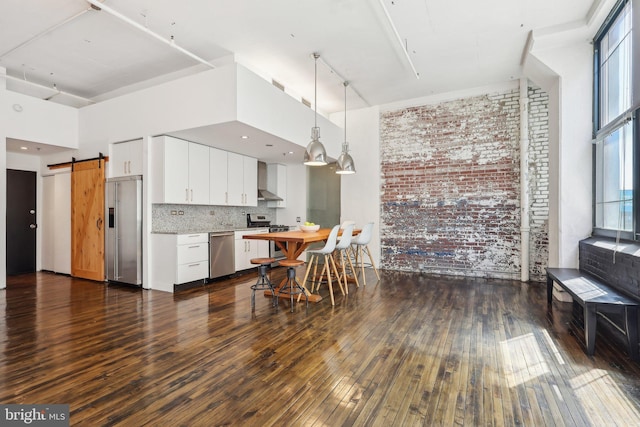 kitchen featuring brick wall, appliances with stainless steel finishes, a barn door, light countertops, and dark wood-type flooring