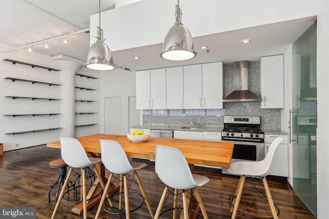 kitchen with wall chimney range hood, track lighting, dark wood finished floors, stainless steel appliances, and backsplash
