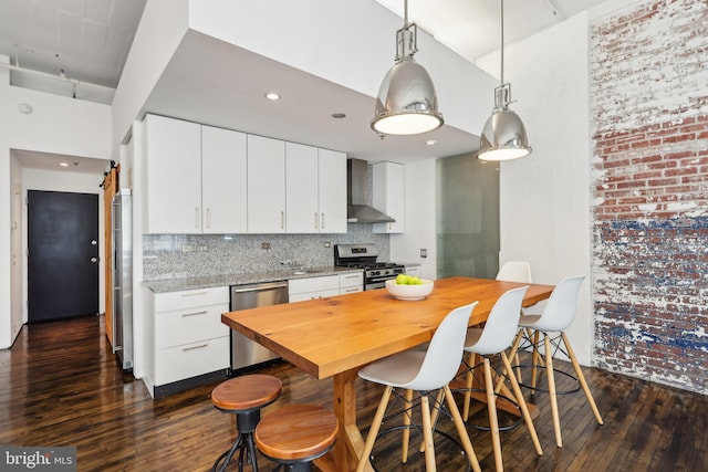 kitchen with backsplash, a kitchen bar, appliances with stainless steel finishes, wall chimney exhaust hood, and dark wood-type flooring