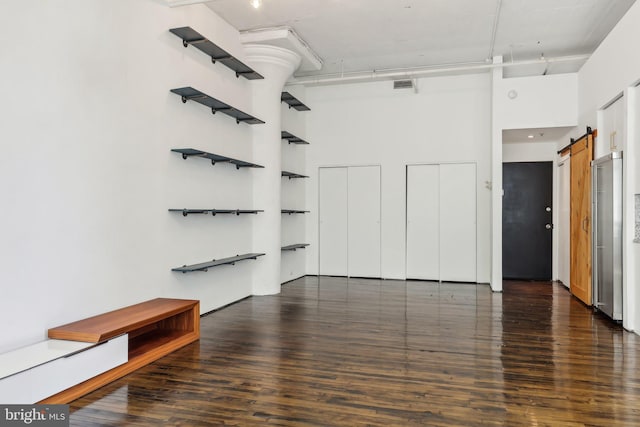 interior space with a high ceiling, visible vents, a barn door, and wood finished floors
