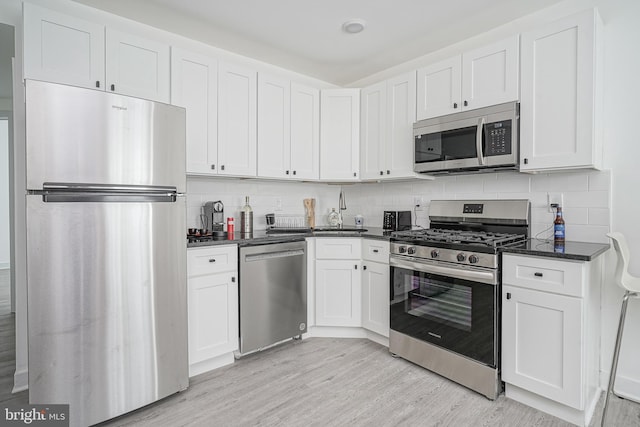 kitchen with decorative backsplash, a sink, white cabinets, stainless steel appliances, and light wood-style flooring