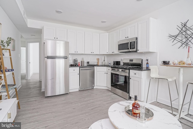 kitchen with decorative backsplash, stainless steel appliances, light wood finished floors, and white cabinets