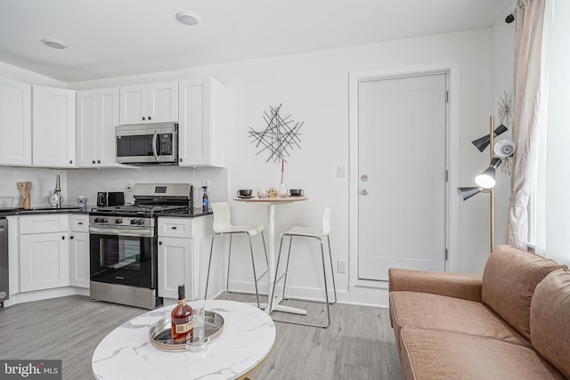 kitchen with white cabinets, appliances with stainless steel finishes, decorative backsplash, and light wood-style flooring