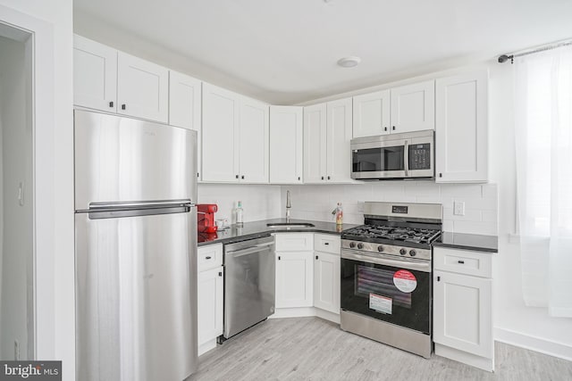 kitchen with light wood-type flooring, a sink, dark countertops, and stainless steel appliances