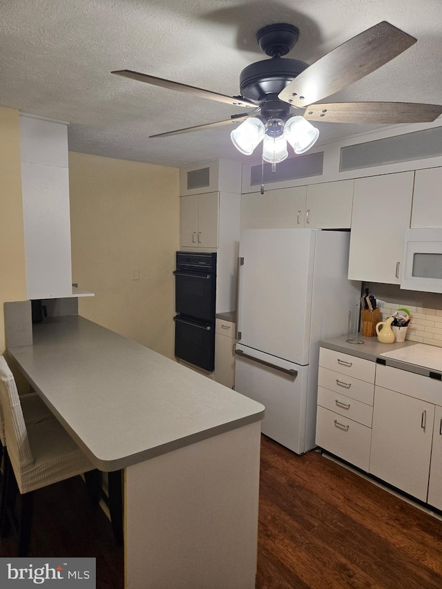 kitchen with a peninsula, white appliances, ceiling fan, dark wood-style floors, and white cabinetry